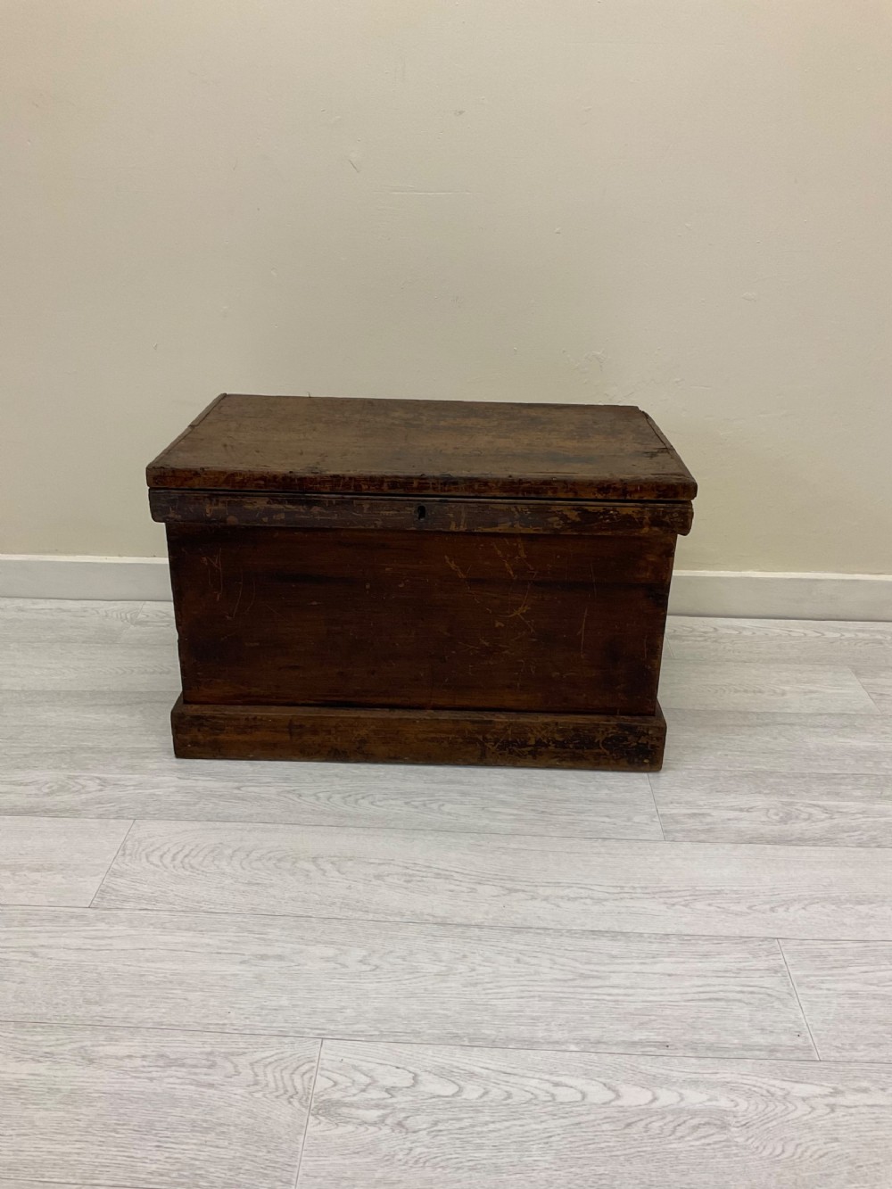 A rectangular 19th-century Victorian pine trunk featuring a dark brown finish, hinged flat lid, central keyhole, and plinth base.