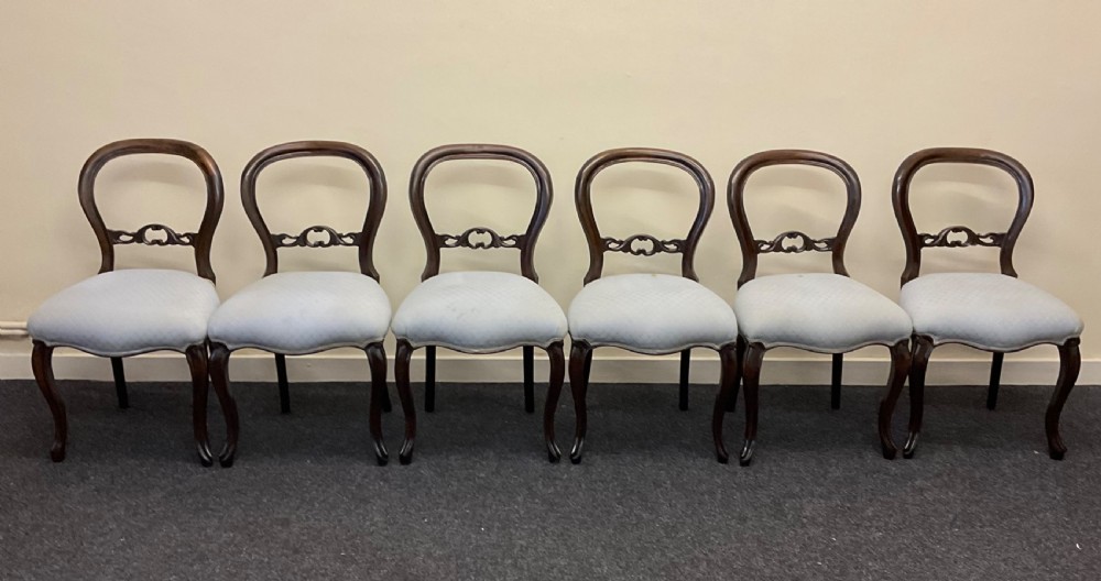 A set of six Victorian mahogany dining chairs featuring rounded balloon backs, central carved splats, light blue upholstered seats, and cabriole front legs.
