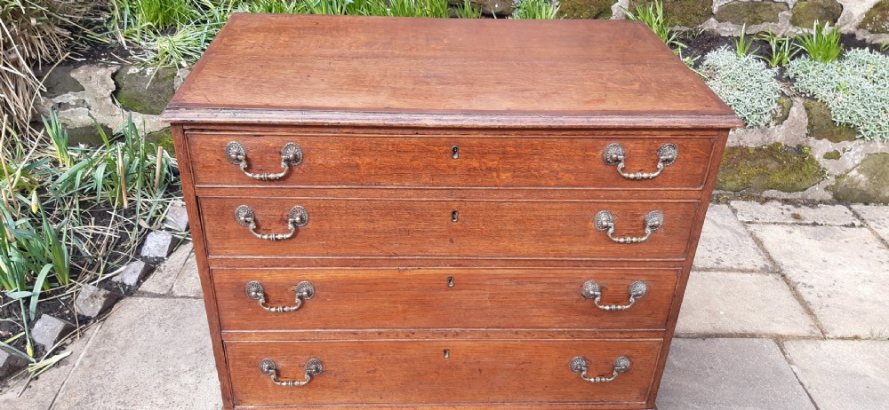 A Georgian oak chest of drawers featuring four full-width drawers with brass handles and keyhole escutcheons, resting on bracket feet. View III