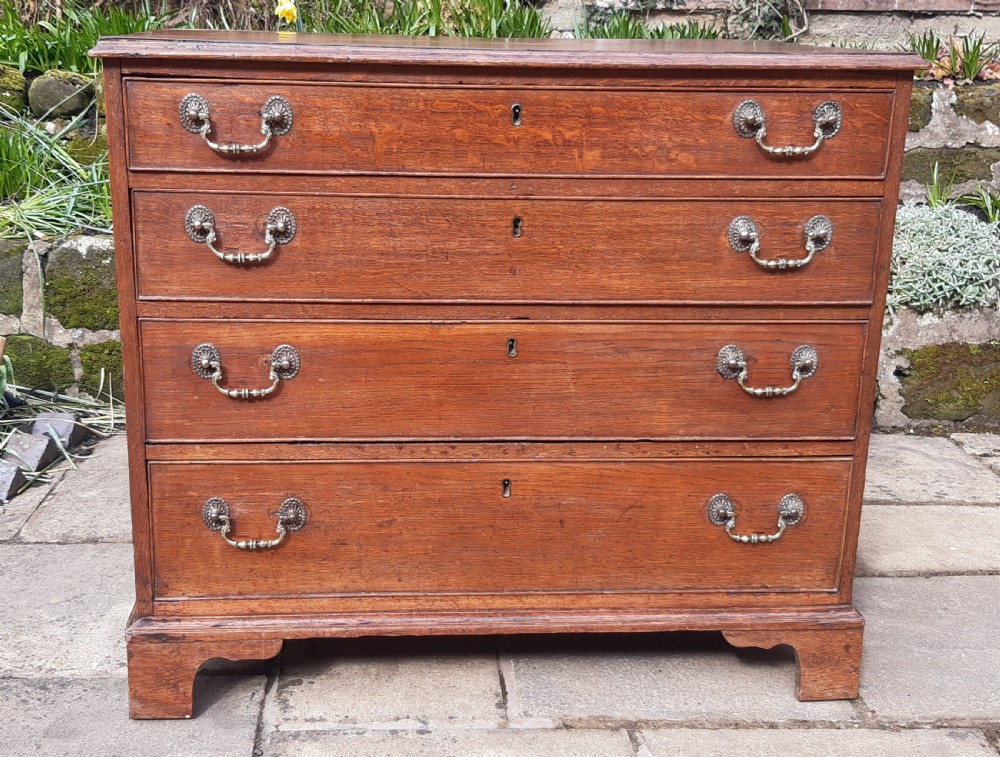 A Georgian oak chest of drawers featuring four full-width drawers with brass handles and keyhole escutcheons, resting on bracket feet.