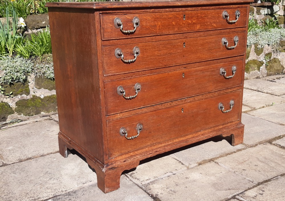 A Georgian oak chest of drawers featuring four full-width drawers with brass handles and keyhole escutcheons, resting on bracket feet. View VI
