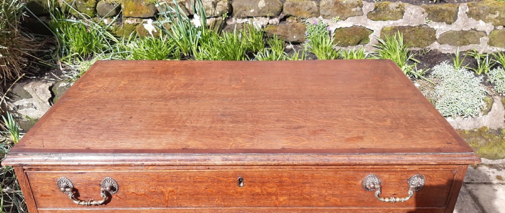 A Georgian oak chest of drawers featuring four full-width drawers with brass handles and keyhole escutcheons, resting on bracket feet. View IX
