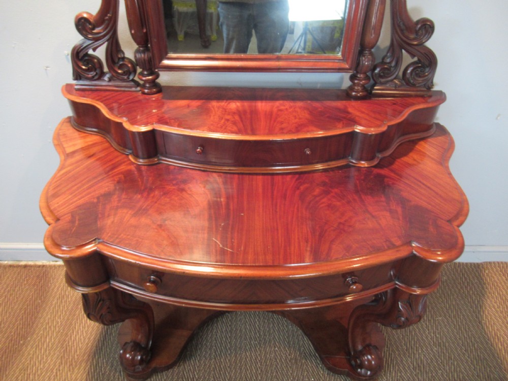 Victorian mahogany duchess dressing table featuring an arched swivel mirror, scroll supports, tier of trinket drawers, and a curved base with carved front legs. View II