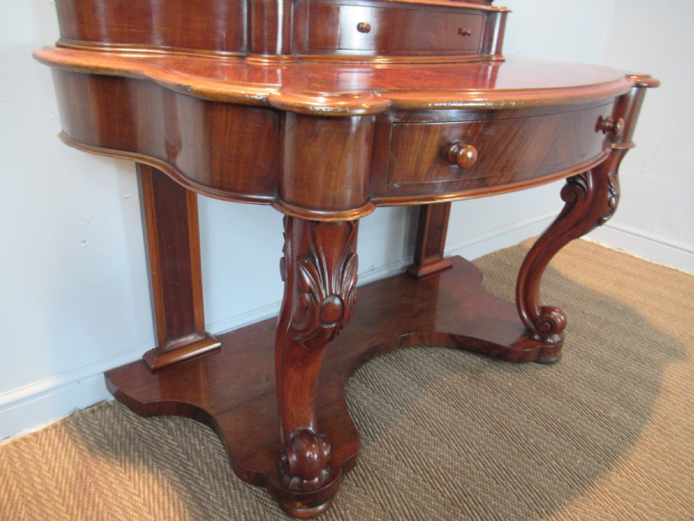 Victorian mahogany duchess dressing table featuring an arched swivel mirror, scroll supports, tier of trinket drawers, and a curved base with carved front legs. View VII