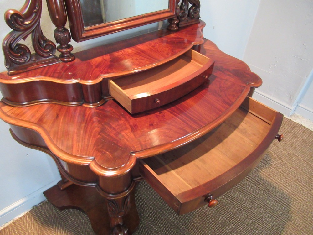 Victorian mahogany duchess dressing table featuring an arched swivel mirror, scroll supports, tier of trinket drawers, and a curved base with carved front legs. View VIII