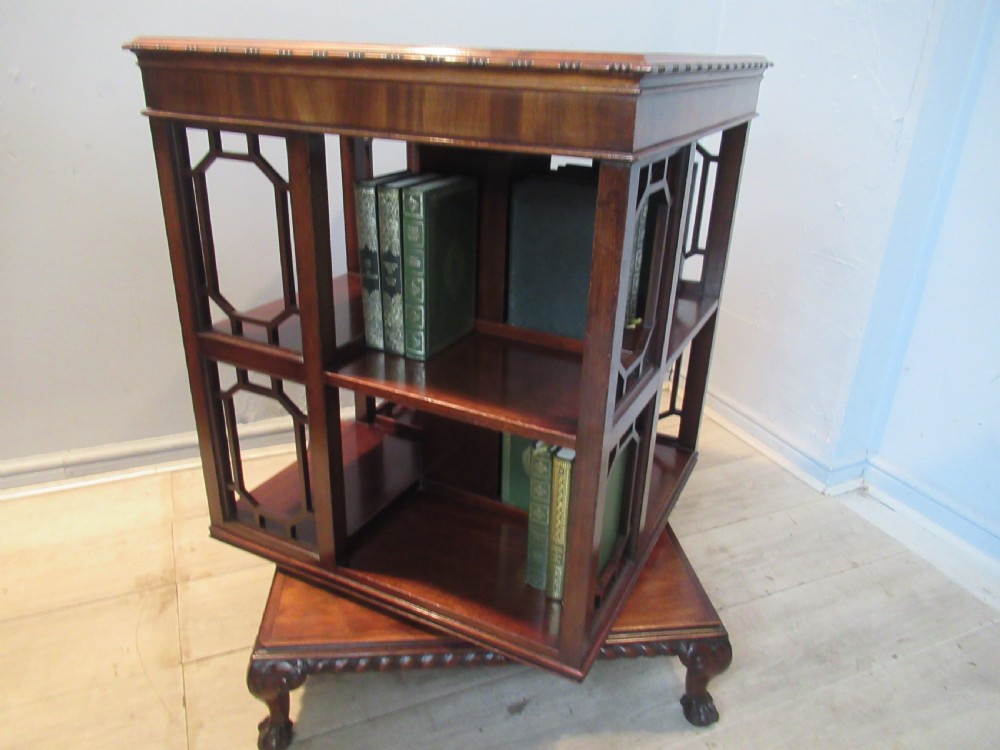 A square dark mahogany revolving bookcase featuring two tiers, fretwork side panels, and carved ball and claw feet.