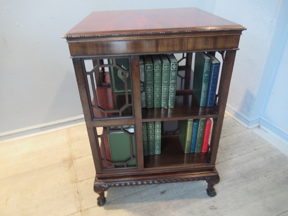 A square dark mahogany revolving bookcase featuring two tiers, fretwork side panels, and carved ball and claw feet. View II