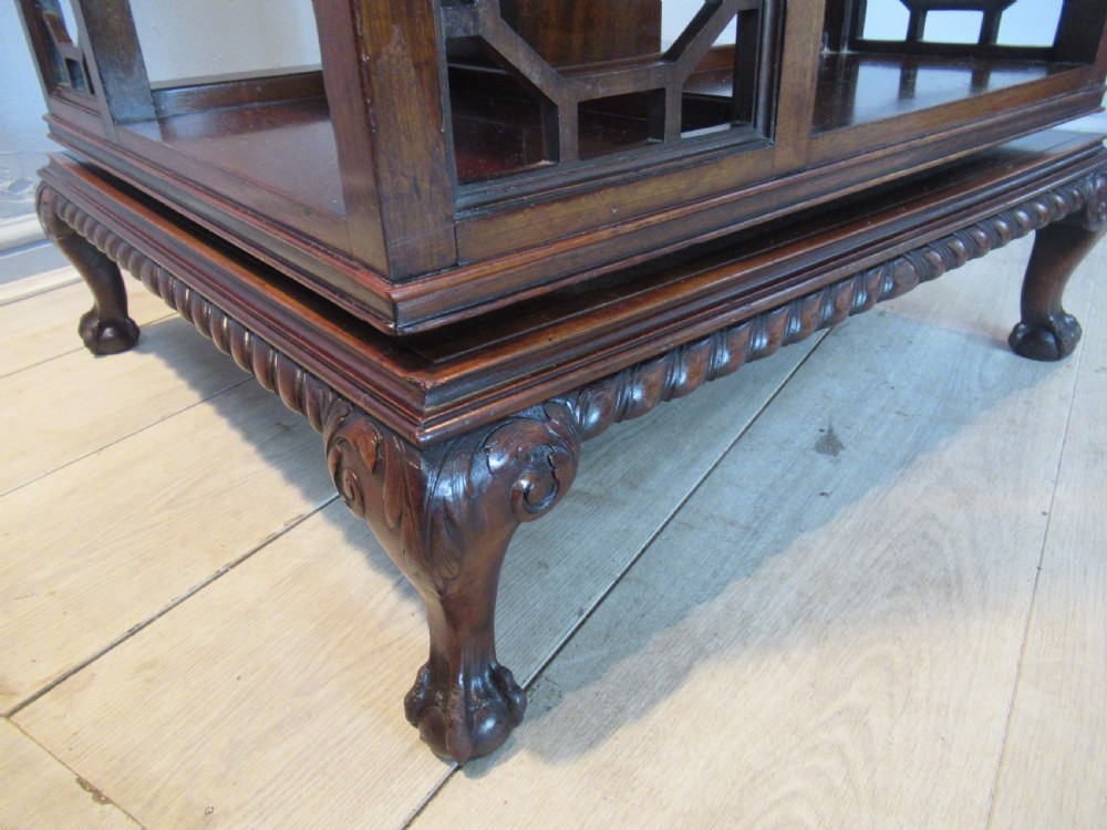 A square dark mahogany revolving bookcase featuring two tiers, fretwork side panels, and carved ball and claw feet. View X