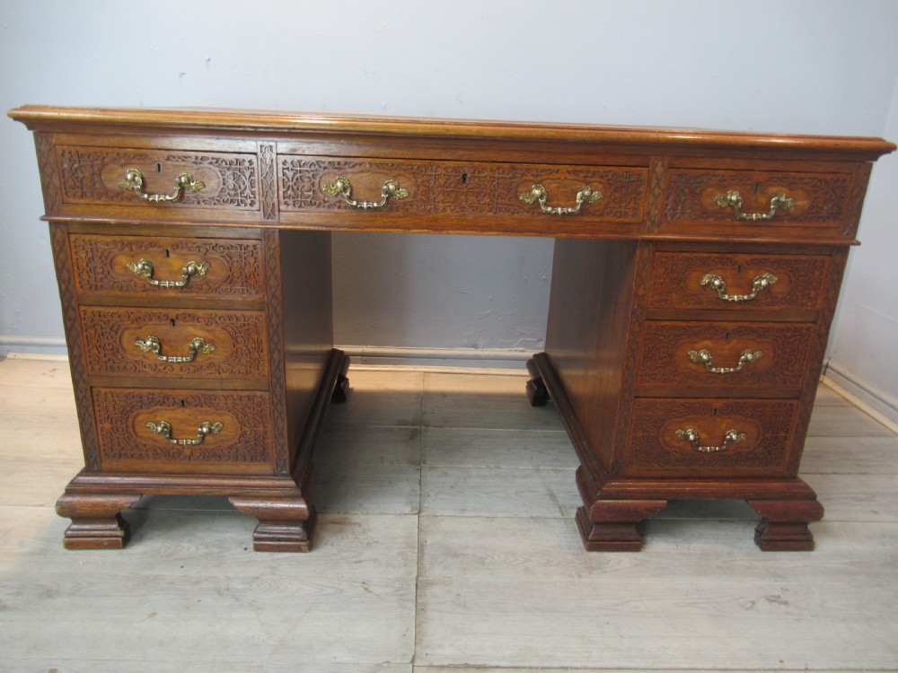 A late Victorian carved oak kneehole pedestal desk featuring nine drawers with relief carving and brass handles.