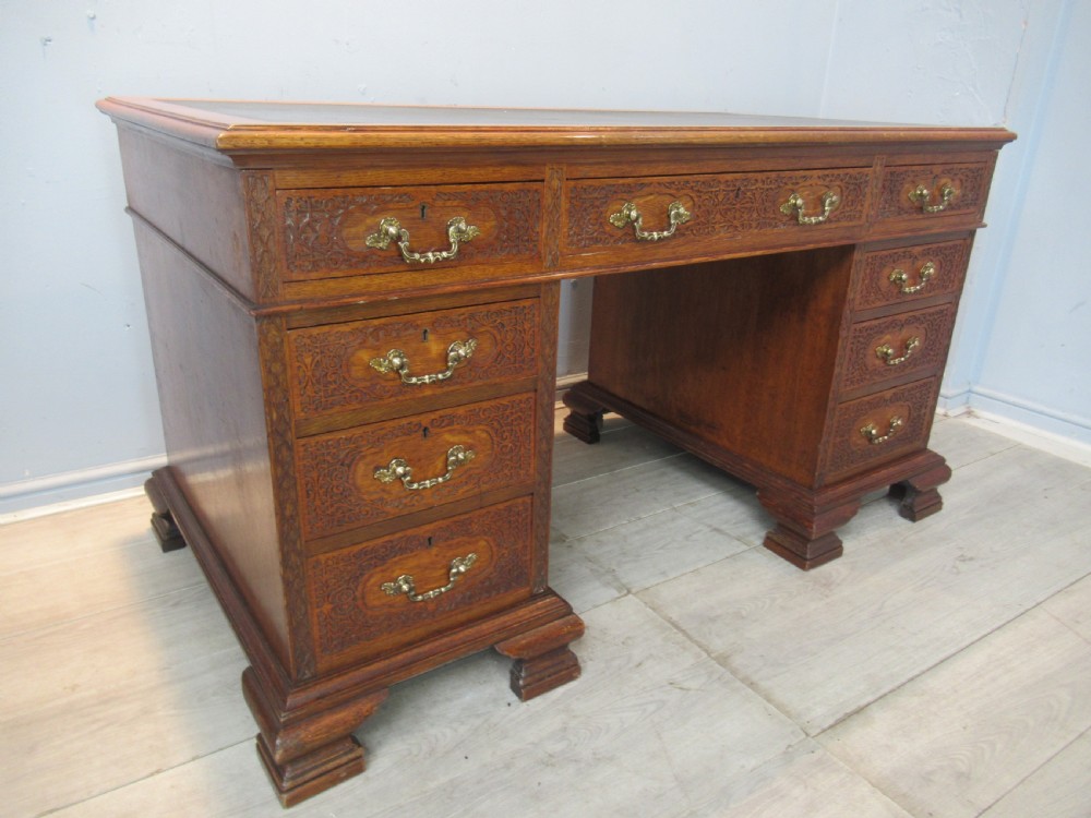 A late Victorian carved oak kneehole pedestal desk featuring nine drawers with relief carving and brass handles. View II