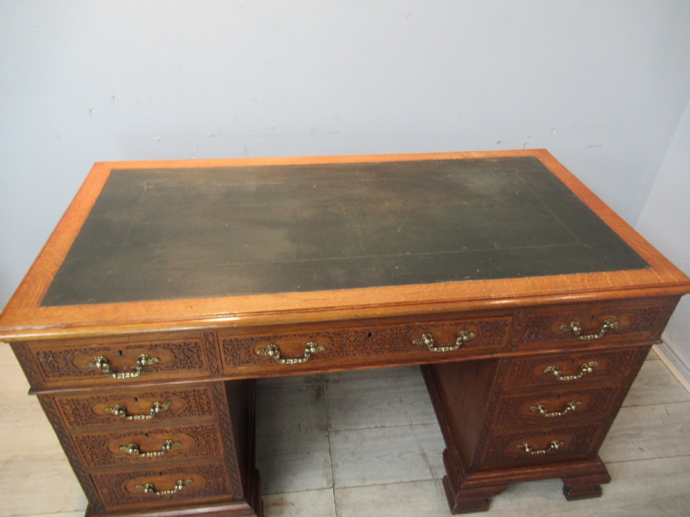 A late Victorian carved oak kneehole pedestal desk featuring nine drawers with relief carving and brass handles. View VI