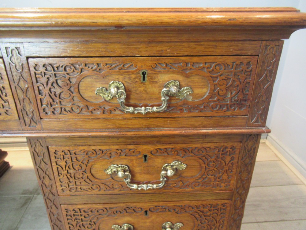 A late Victorian carved oak kneehole pedestal desk featuring nine drawers with relief carving and brass handles. View IX