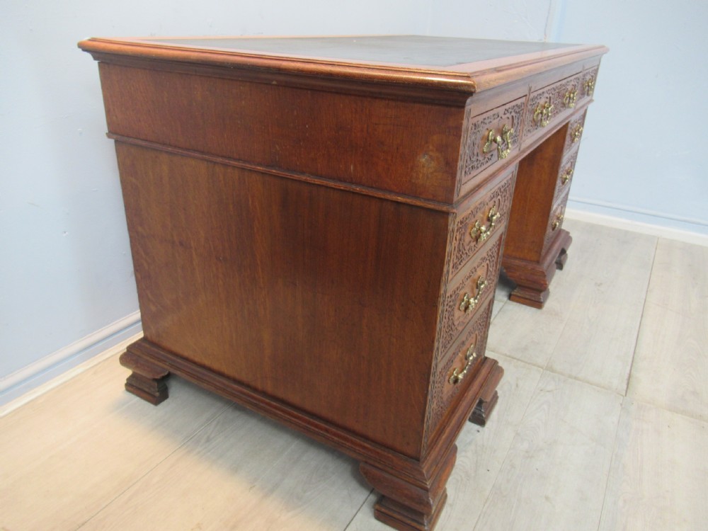 A late Victorian carved oak kneehole pedestal desk featuring nine drawers with relief carving and brass handles. View XI