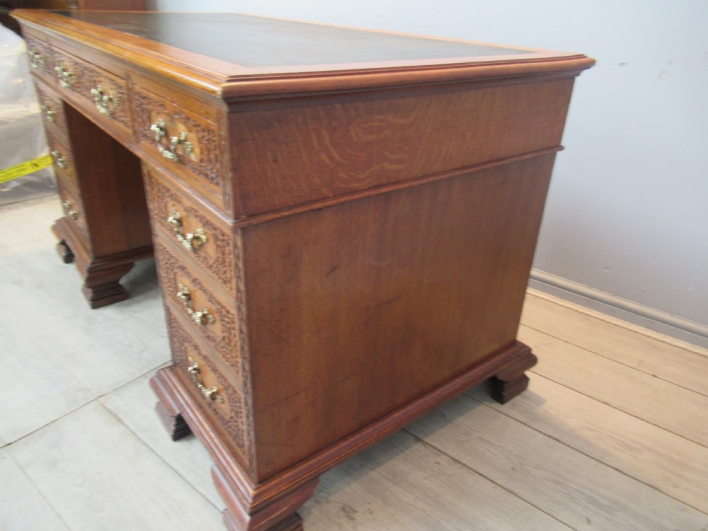 A late Victorian carved oak kneehole pedestal desk featuring nine drawers with relief carving and brass handles. View XII