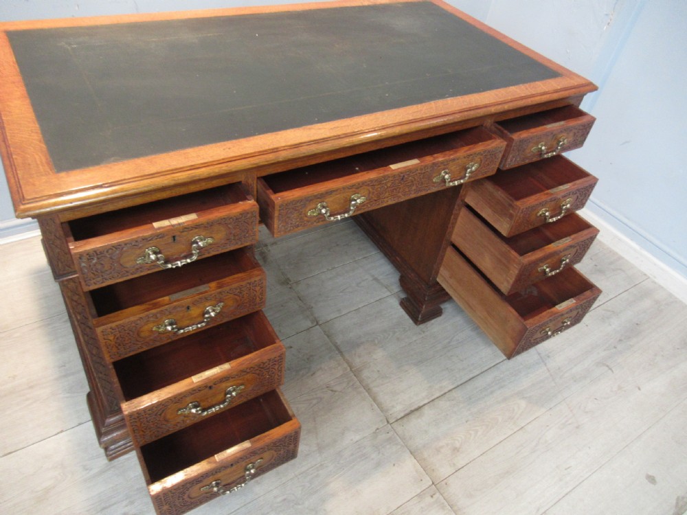A late Victorian carved oak kneehole pedestal desk featuring nine drawers with relief carving and brass handles. View XIII