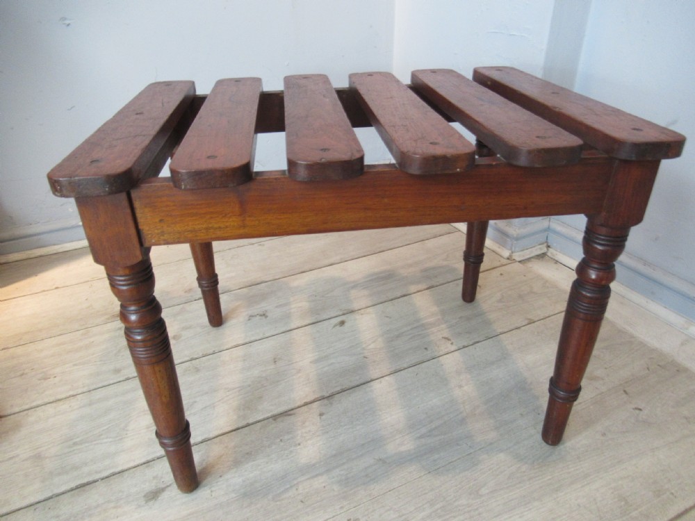 A late Victorian mahogany luggage stand featuring six rounded slatted top rails supported by a sturdy timber frame and four turned legs.