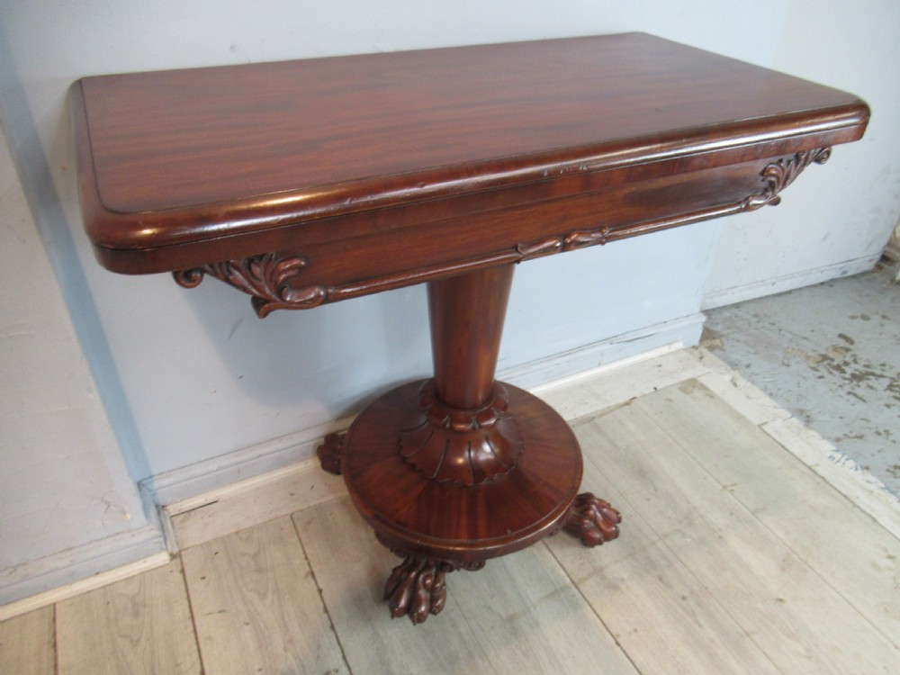 A Victorian mahogany card table featuring a rectangular fold-over top, a central turned pedestal, and carved paw feet on a circular platform base.