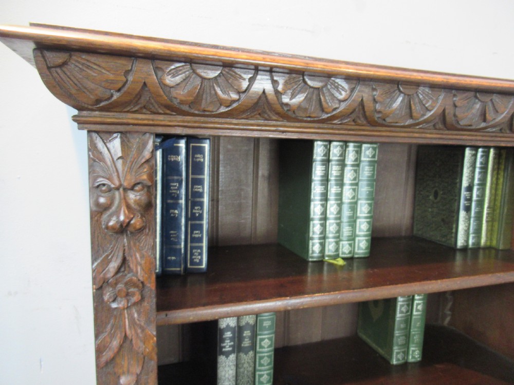 A Victorian carved oak open bookcase featuring four wide shelves flanked by carved foliate and lion head pilasters. View X