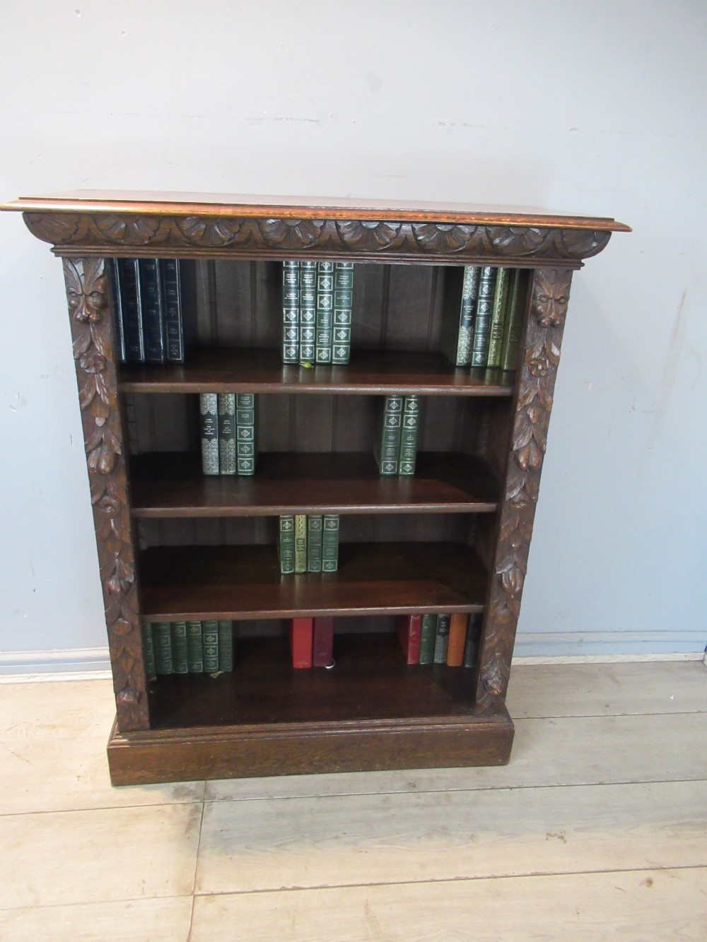 A Victorian carved oak open bookcase featuring four wide shelves flanked by carved foliate and lion head pilasters. View II