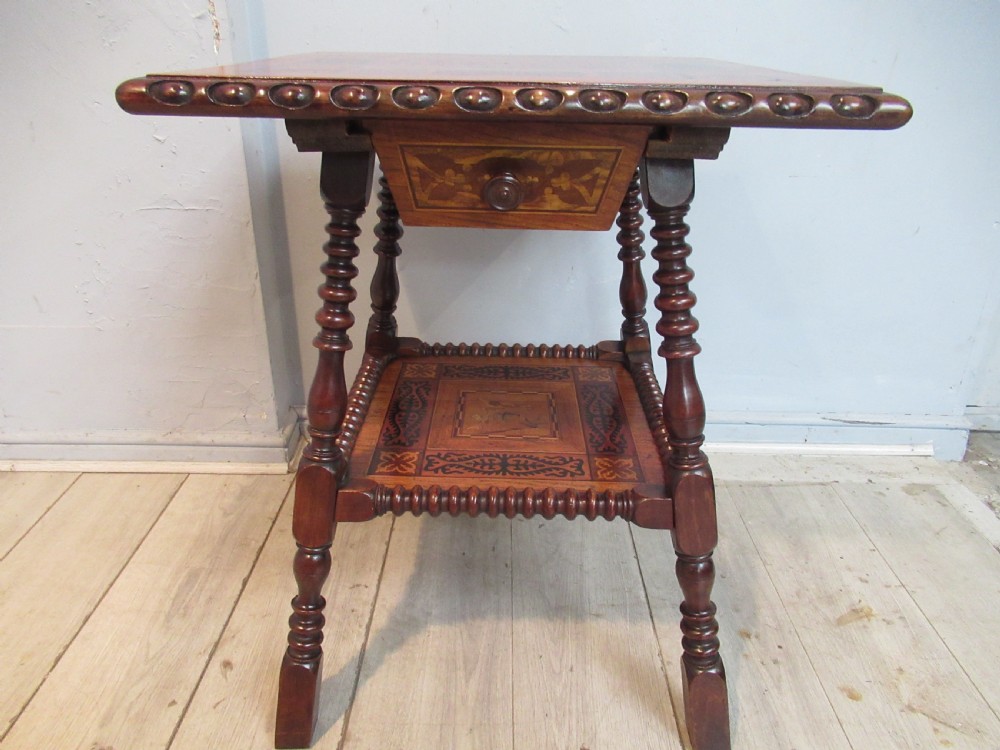 A 19th-century rich brown wood side table featuring a single drawer with marquetry inlay, carved bead edging, turned legs, and an inlaid lower shelf.