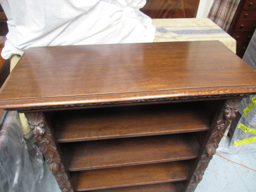 A Victorian carved oak open bookcase featuring four wide shelves flanked by carved foliate and lion head pilasters. View V