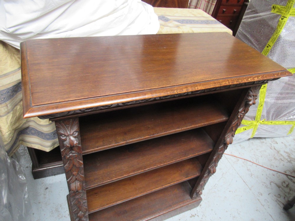 A Victorian carved oak open bookcase featuring four wide shelves flanked by carved foliate and lion head pilasters. View XIII