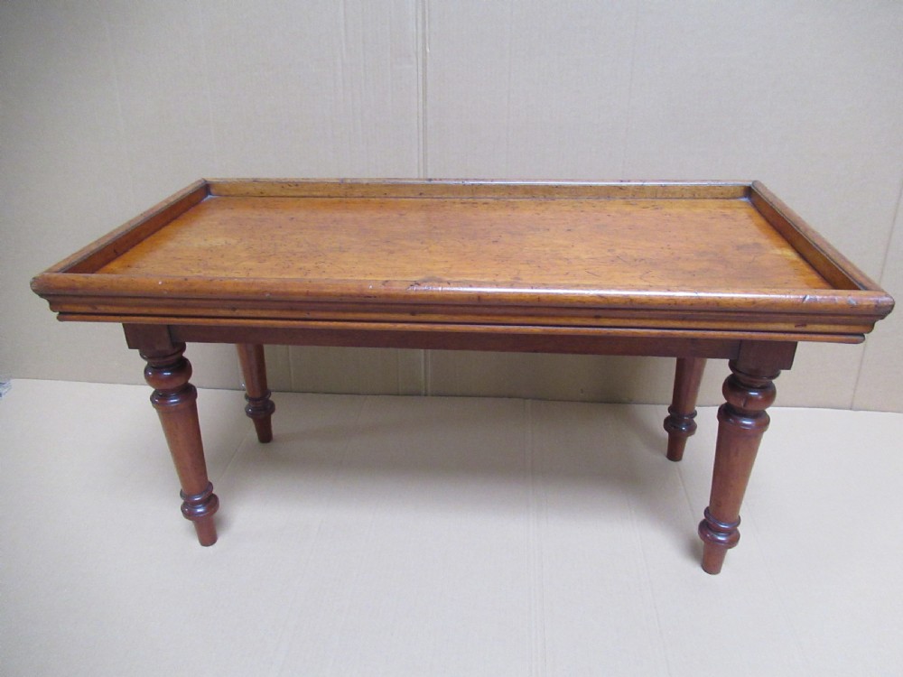 A low 19th-century mahogany folding campaign travel table featuring a tray top rim and turned legs.