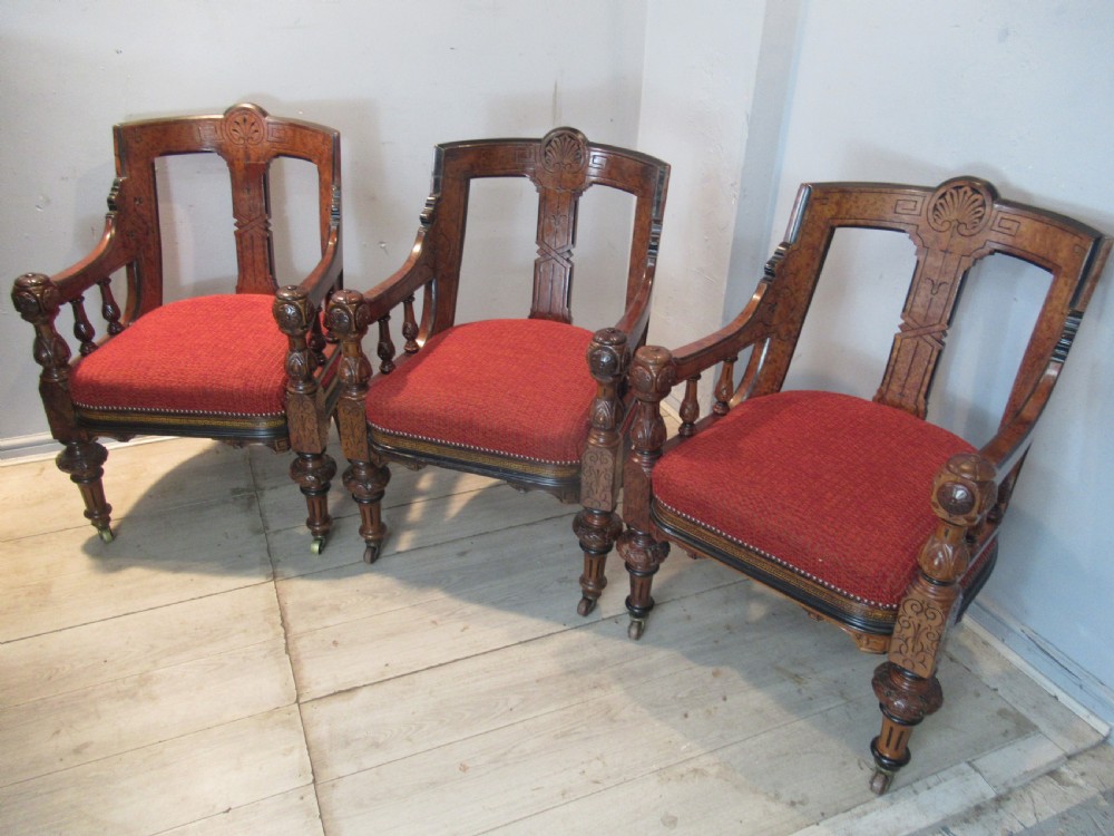 A set of three Victorian mahogany open armchairs with carved backrests, red upholstered seats, and turned front legs on brass castors.
