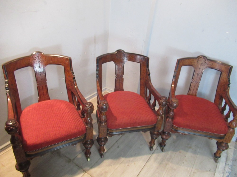 A set of three Victorian mahogany open armchairs with carved backrests, red upholstered seats, and turned front legs on brass castors. View II