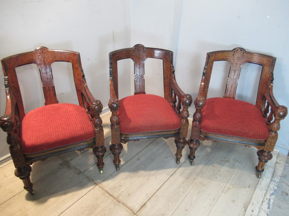 A set of three Victorian mahogany open armchairs with carved backrests, red upholstered seats, and turned front legs on brass castors. View XV