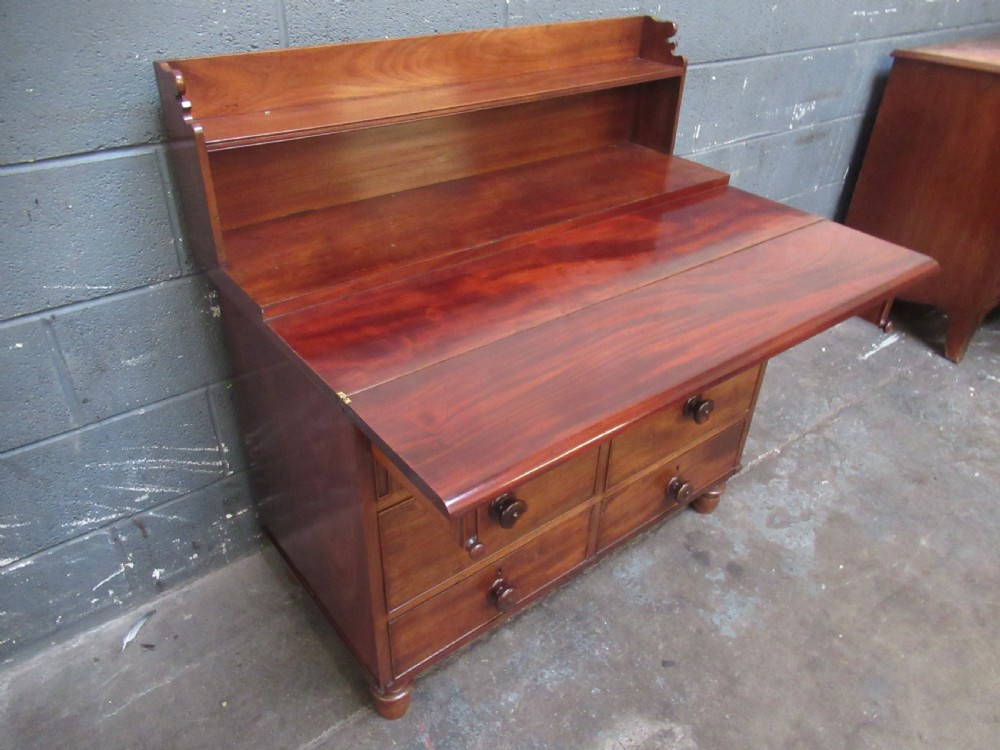 A Victorian mahogany chest of drawers featuring a fold-out top surface, an upper open shelf gallery, and turned wooden knobs.