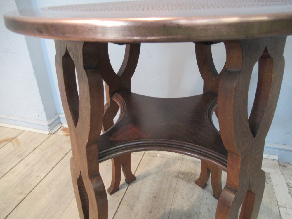 A circular Arts and Crafts oak side table featuring a hammered copper top insert and stylized shaped legs with a lower cross shelf. View XI