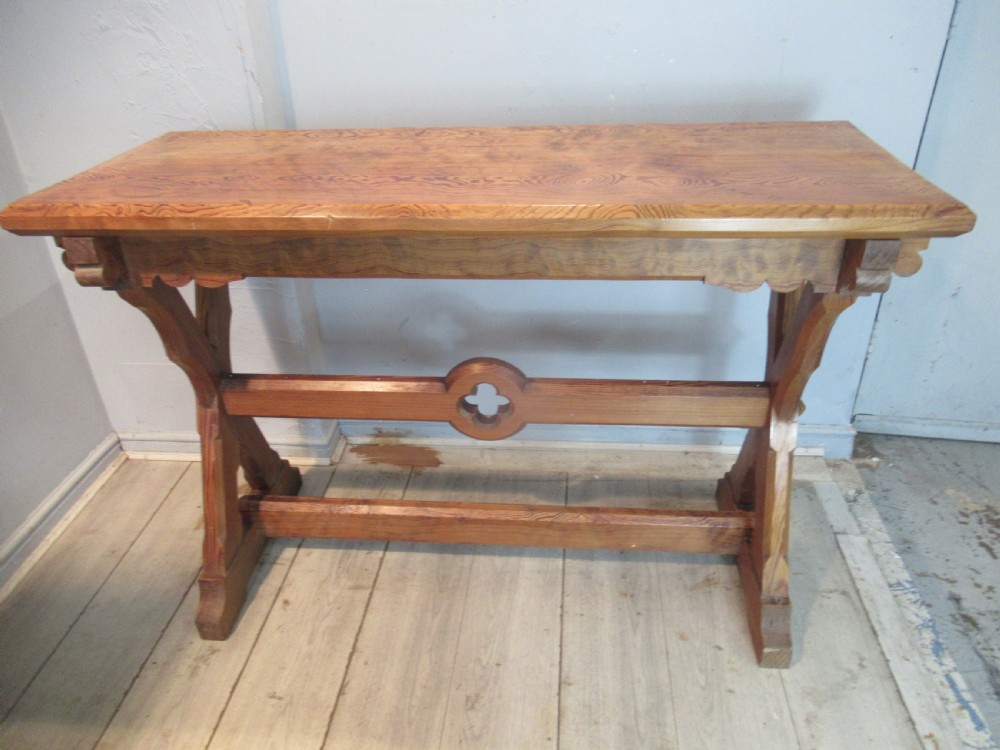A Victorian pitch pine side table with a rectangular top, scalloped apron, and trestle supports joined by a stretcher with a carved quatrefoil motif.