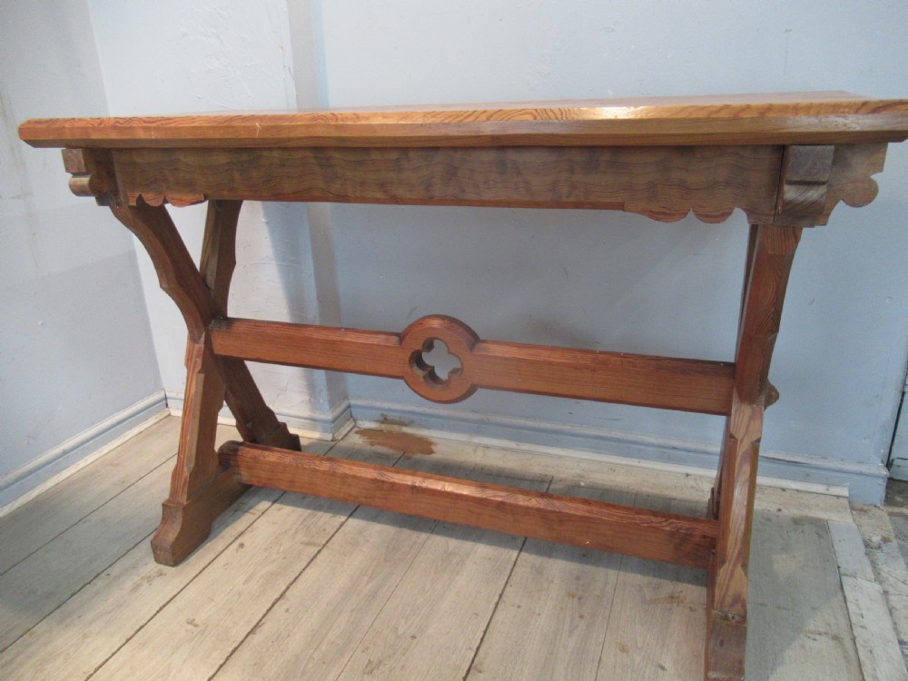 A Victorian pitch pine side table with a rectangular top, scalloped apron, and trestle supports joined by a stretcher with a carved quatrefoil motif. View II