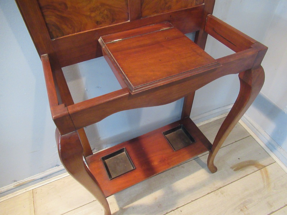 An antique walnut hall stand featuring an integrated mirror, multiple brass coat hooks, a central glove box, and a lower umbrella rack with metal drip trays. View VI