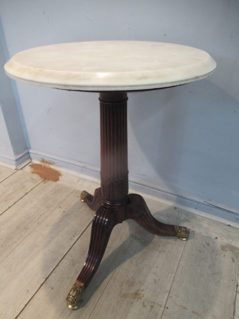 A Regency period circular table featuring a white marble top supported by a reeded mahogany pedestal on a splayed tripod base with brass feet.