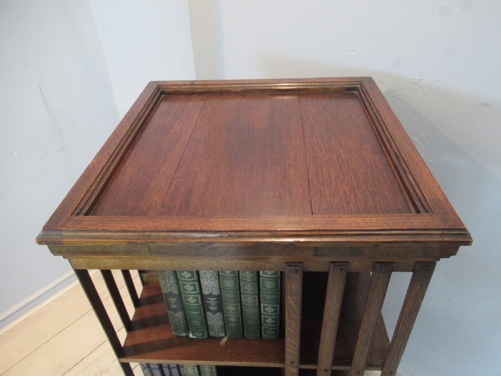 A tall Edwardian solid oak revolving bookcase featuring four open tiers, slatted sides, and a moulded square top. View VI