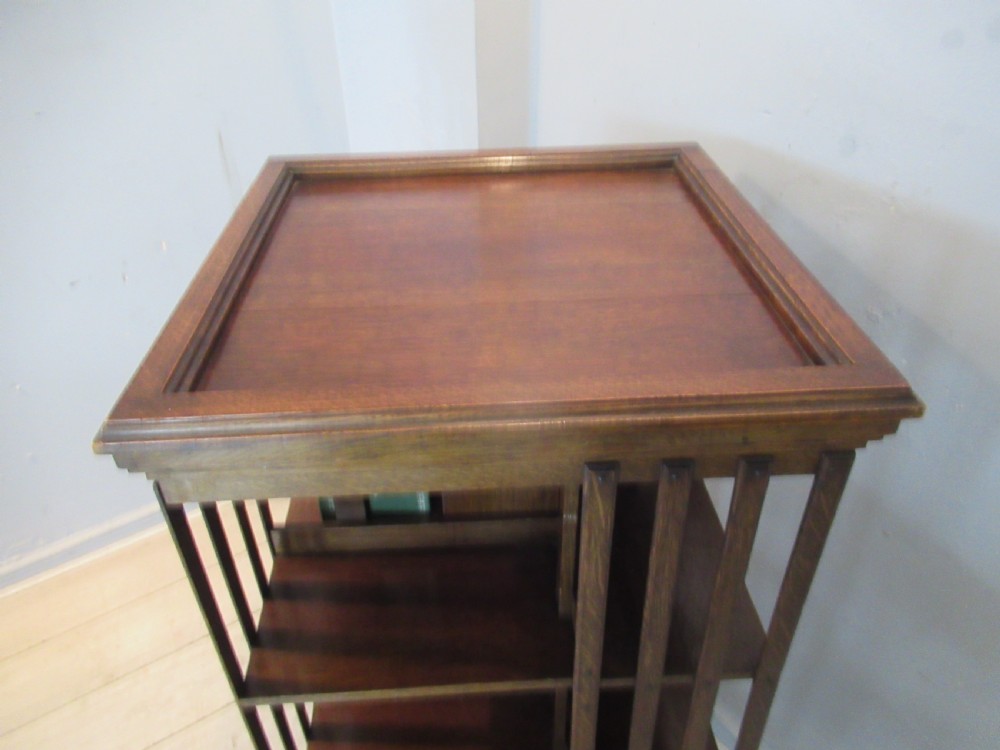 A tall Edwardian solid oak revolving bookcase featuring four open tiers, slatted sides, and a moulded square top. View VII