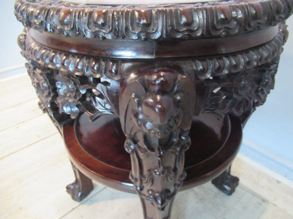 A circular dark carved hardwood side table featuring an inset marble top, pierced floral apron, lower tier shelf, and legs terminating in claw feet. View V