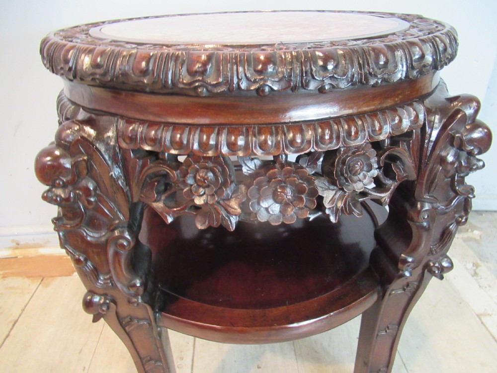 A circular dark carved hardwood side table featuring an inset marble top, pierced floral apron, lower tier shelf, and legs terminating in claw feet. View VI