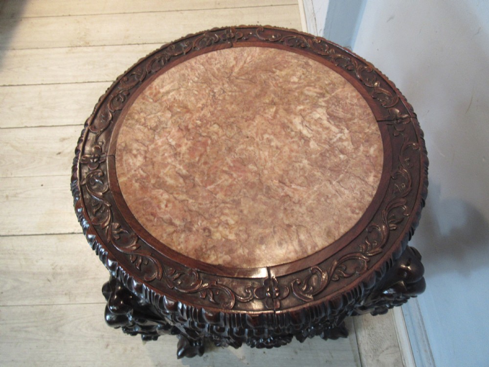 A circular dark carved hardwood side table featuring an inset marble top, pierced floral apron, lower tier shelf, and legs terminating in claw feet. View IX