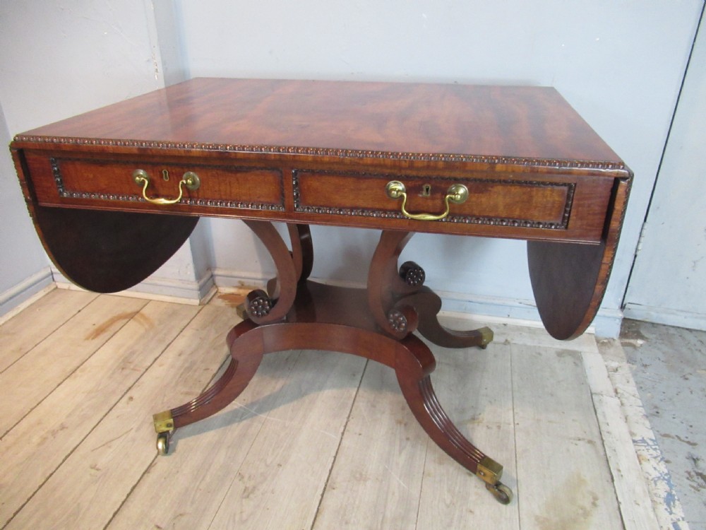An early 19th-century mahogany sofa table featuring two drop leaf flaps, two front drawers with brass handles, twin scroll supports, and reeded legs with brass castors. View II