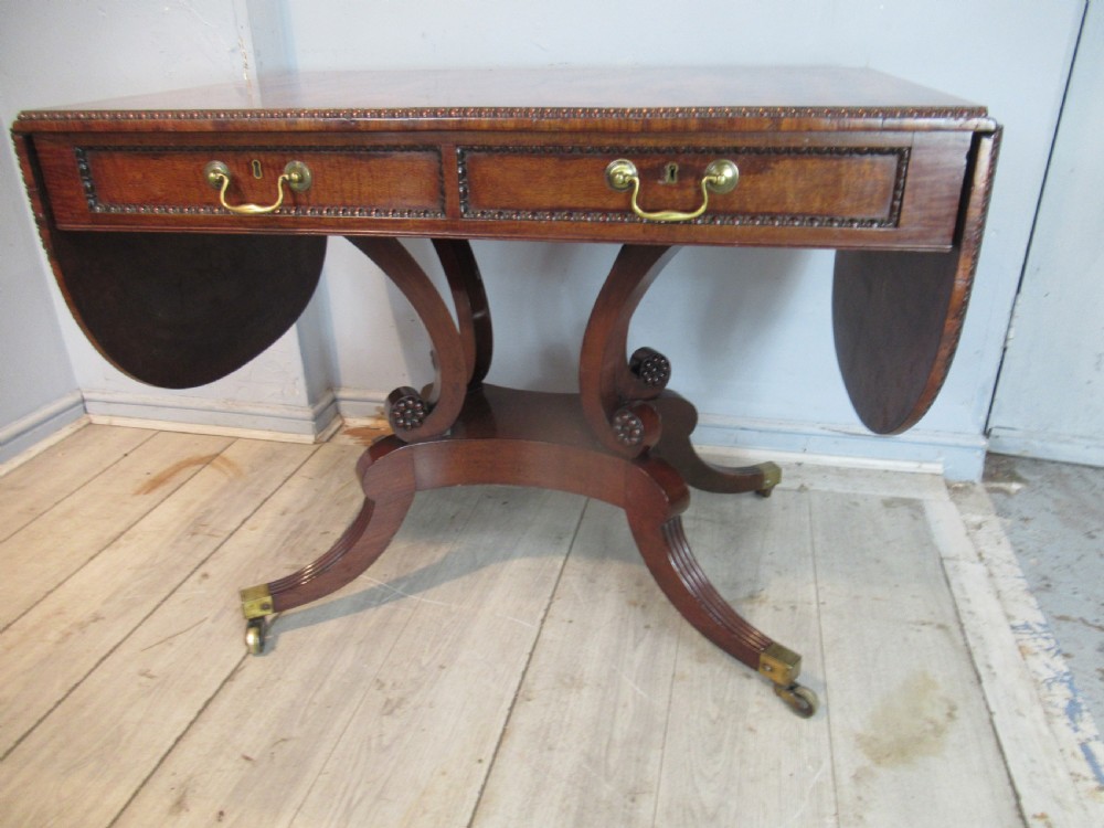 An early 19th-century mahogany sofa table featuring two drop leaf flaps, two front drawers with brass handles, twin scroll supports, and reeded legs with brass castors. View III