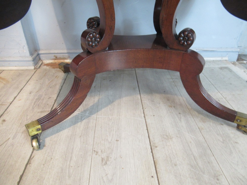 An early 19th-century mahogany sofa table featuring two drop leaf flaps, two front drawers with brass handles, twin scroll supports, and reeded legs with brass castors. View V