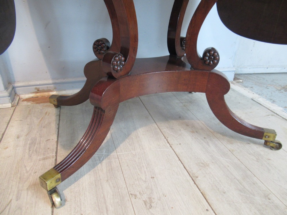 An early 19th-century mahogany sofa table featuring two drop leaf flaps, two front drawers with brass handles, twin scroll supports, and reeded legs with brass castors. View VI
