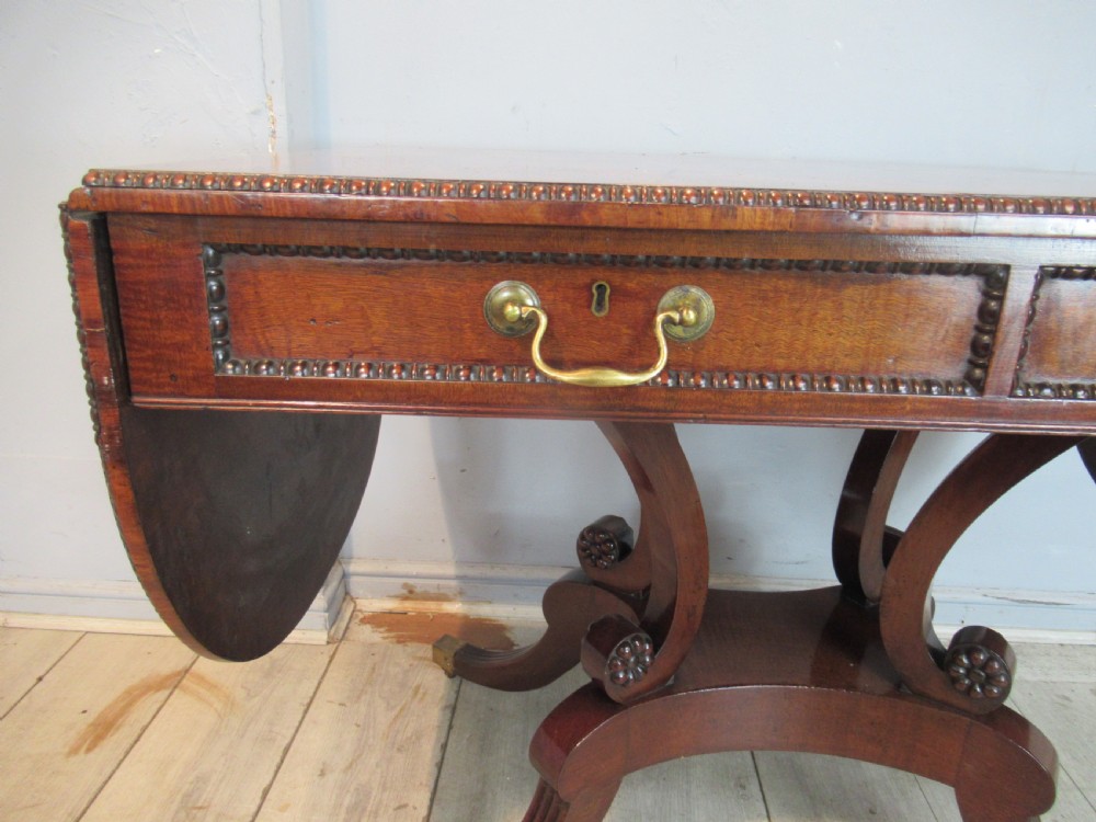 An early 19th-century mahogany sofa table featuring two drop leaf flaps, two front drawers with brass handles, twin scroll supports, and reeded legs with brass castors. View VIII