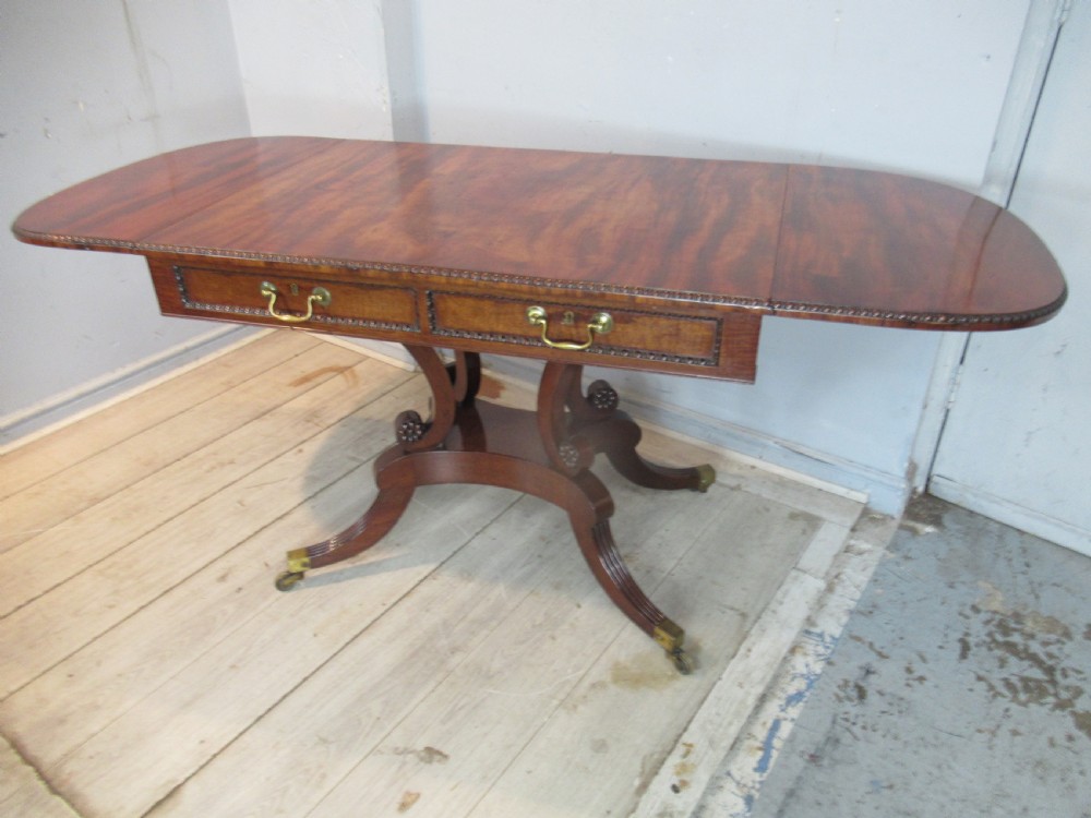 An early 19th-century mahogany sofa table featuring two drop leaf flaps, two front drawers with brass handles, twin scroll supports, and reeded legs with brass castors. View XIV