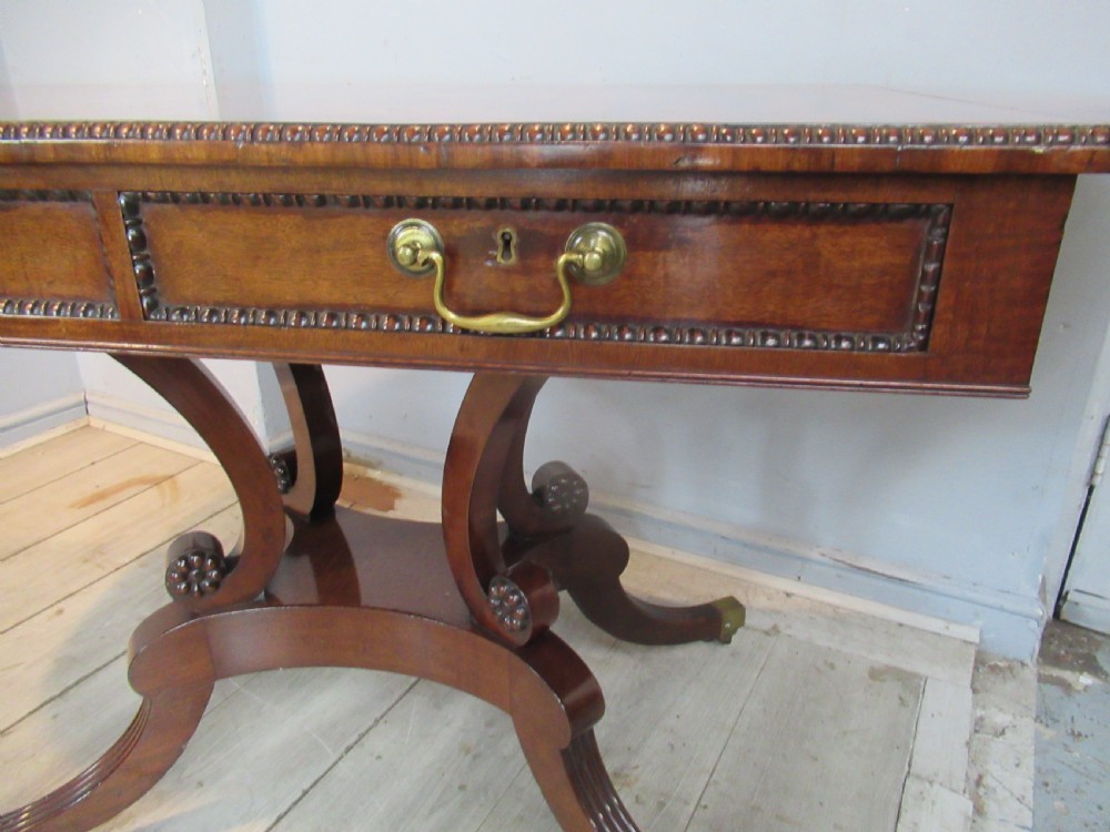 An early 19th-century mahogany sofa table featuring two drop leaf flaps, two front drawers with brass handles, twin scroll supports, and reeded legs with brass castors. View XVII