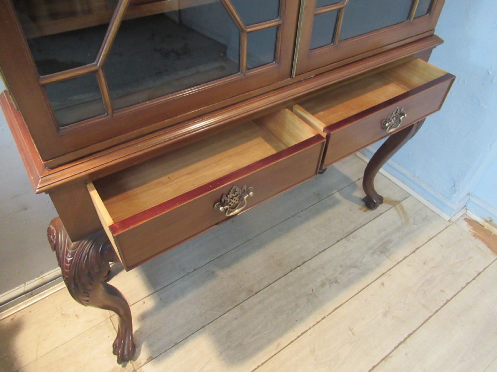 A Chippendale style mahogany glazed bookcase featuring geometric astragal doors, lower drawers, and carved cabriole legs ending in ball-and-claw feet. View X