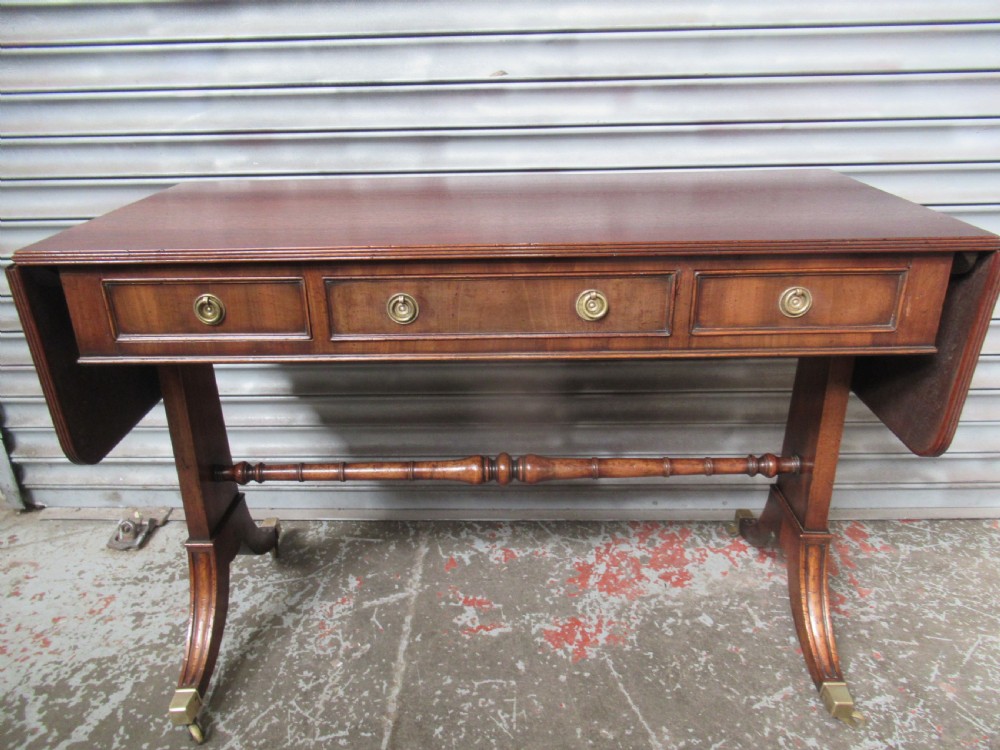 A mahogany sofa table featuring drop-leaf sides, front drawers with brass ring handles, a turned stretcher, and splayed sabre legs with brass castors.